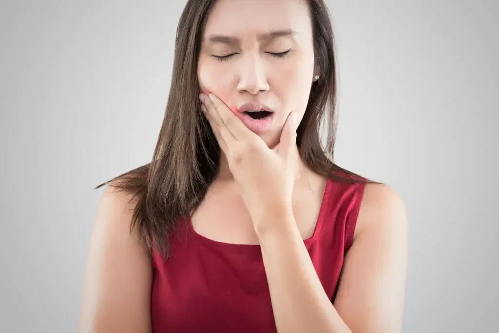 Mulher com a mão no rosto sentindo dor de dente do siso
